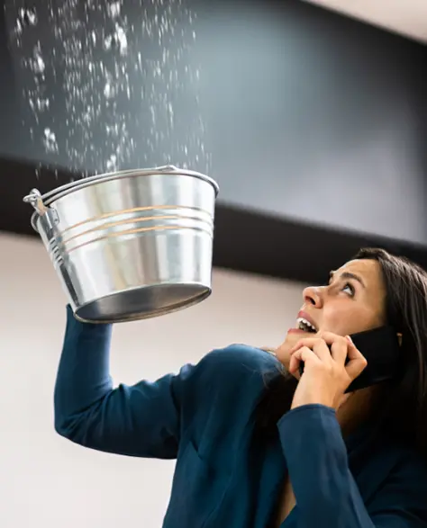 Water Damage Restoration Contractors in East Meadow, NY - A Woman Calling Someone to Fix a Leak, Holding a Bucket Under the Leak to Catch the Water