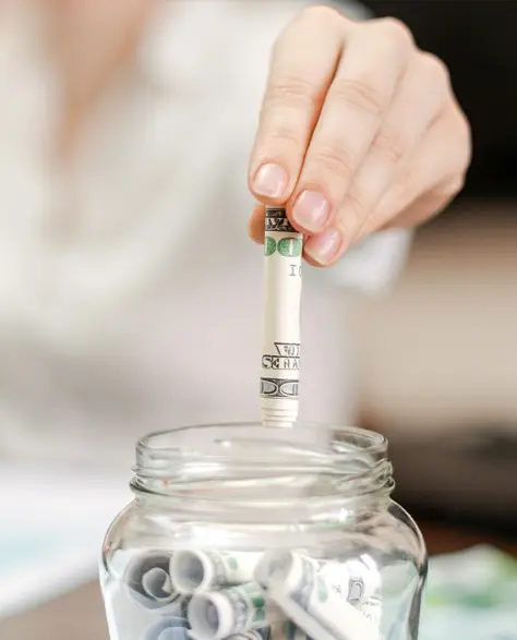 Spray Foam Insulation Contractors in Douglaston–Little Neck, NY - A Woman Putting Rolled Up Bills in a Savings Jar<br />
