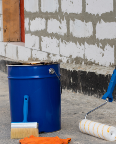 Water Damage Restoration Contractors in Bayside, NY - A bucket of paint with a brush, a roller and a pair of orange gloves on the side 