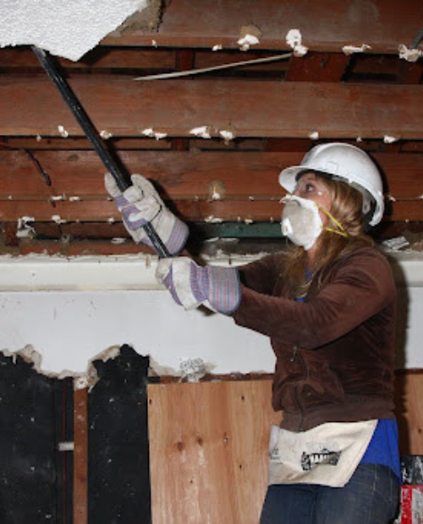 Water Damage Restoration Contractors in Corona, NY - A woman weaning a mask, gloves and a hard hat cleaning mold from an infested roof<br />
