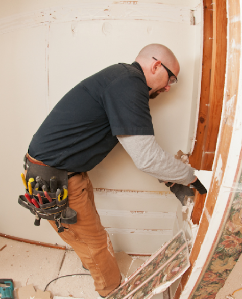 Water Damage Restoration Contractors in Flushing, NY: A man in overalls and a tool belt fixing a wall with water damage 