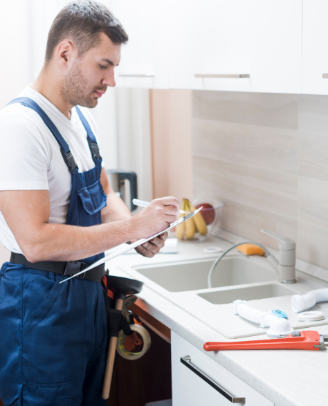 Water Damage Restoration Contractors in Jackson Heights, NY - A Water Damage Restoration Tech at a Homeowner's Kitchen Sink Writing Something on a Clipboard<br />
