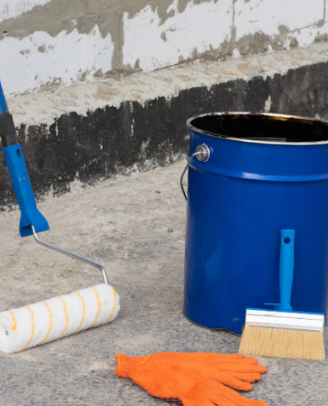 Water Damage Restoration Contractors in Douglaston–Little Neck, NY - Waterproofing Sealant in a Bucket Next to Gloves and a Roller
