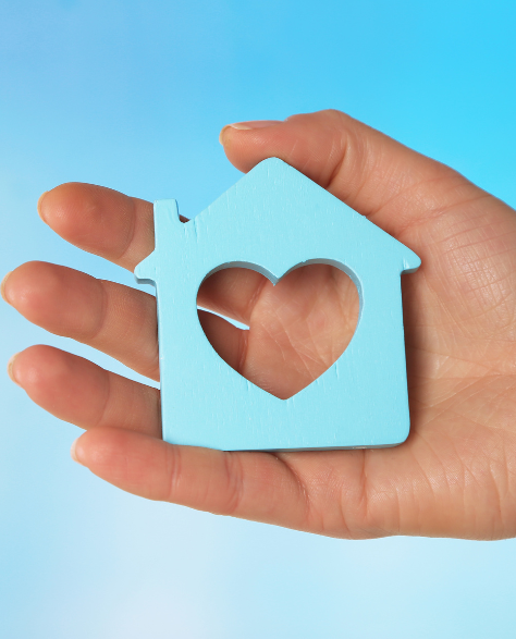 Water Damage Restoration Contractors in Fresh Meadows, NY - A Man’s Hand with a Blue House Cut Out of Paper and a Heart Cut in the Center<br />
