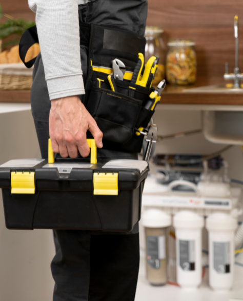 Water Damage Restoration Contractors in Ridgewood, NY - A Man in Front of a Customer’s Kitchen Sink Carrying a Black and Yellow Toolbox<br />
