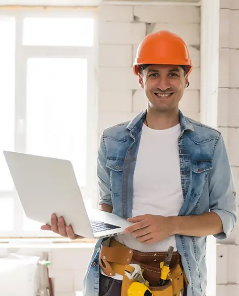 Water Damage Restoration Contractors in Lindenhurst, NY - A Happy Contractor Is Smiling While Holding a Laptop and Wearing a Tool Belt With Suspenders
