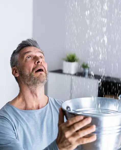 top-rated-water-damage-restoration-contractors-in-Lindenhurst-ny-1.9 Water Damage Restoration Contractors in Lindenhurst, NY - Man holding a steel pail under a leaking roof looking distraught.