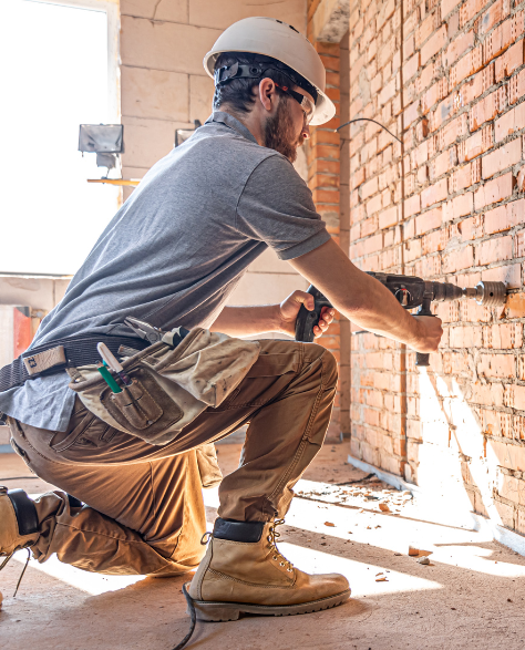 Foundation Repair Contractors in Central Islip, NY - A Man Drilling Into a Wall that the Foundation Has Damaged<br />
