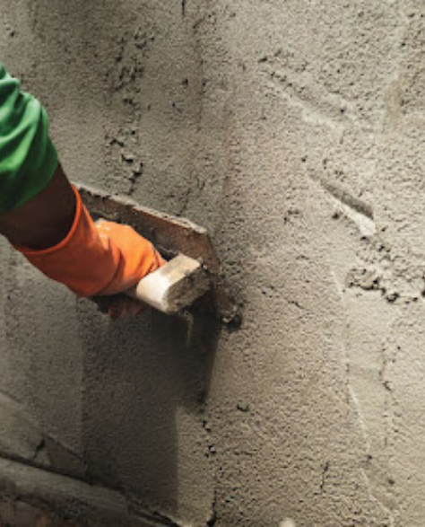 Foundation Repair Contractors in Commack, NY - A Man Using a Trowel to Apply Waterproofing Cement to the Outside of the Foundation<br />
