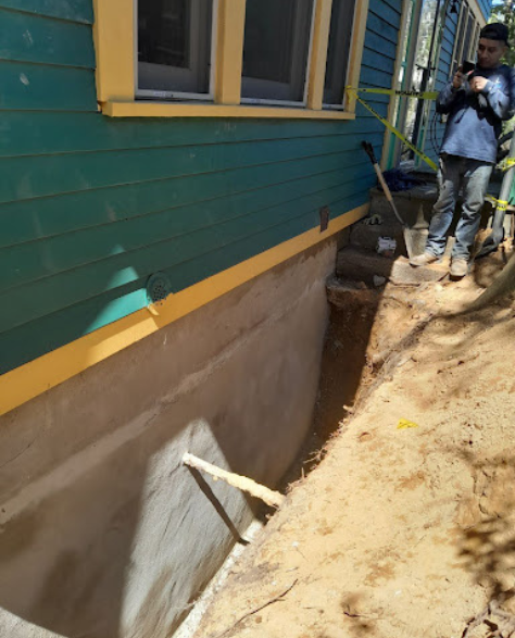Foundation Repair Contractors in Glen Cove, NY - Zavza Seal Foundation Specialists Standing Near a Trench Dug Around a House Foundation to Repair Cracks<br />
