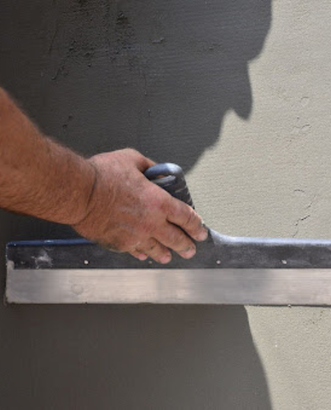 Foundation Repair Contractors in Brooklyn Heights, NY - A Man Using a Trowel to Smooth Out Cement on the Outside of a Foundation<br />
