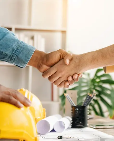 Water Damage Restoration Contractors in Long Island City, NY - A construction worker and a homeowner shaking hands on a deal over a table with hard hats