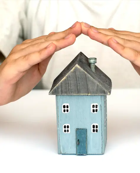 Water Damage Restoration Contractors in Richmond Hill, NY - A Man at a Table with His Hands Cupped Over a House Model in a Roof Shape