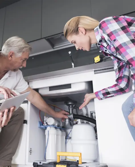 Water Damage Restoration Contractors in South Ozone Park, NY - A Water Damage Restoration Technician Pointing Out Something Under the Kitchen Sink to Homeowners