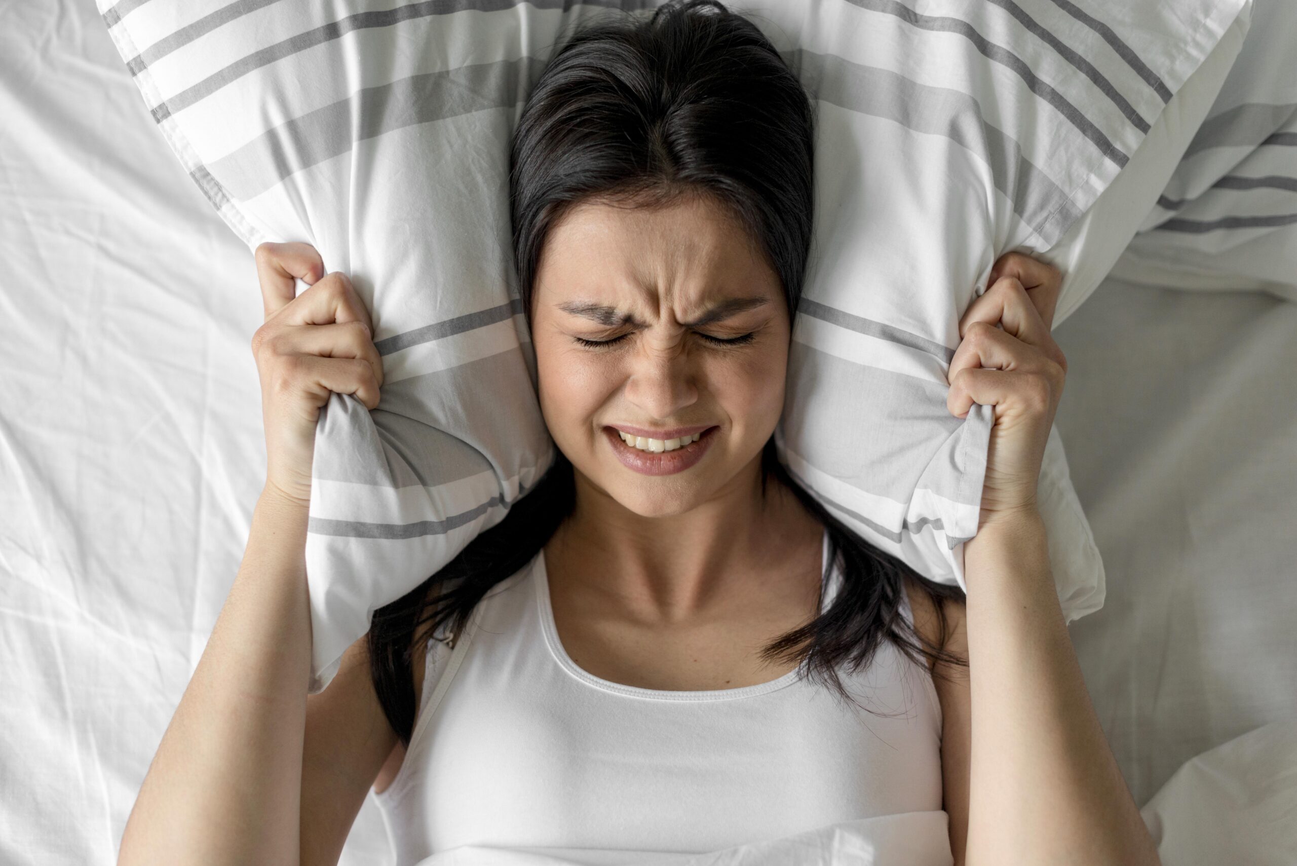 10 warning signs of mold toxicity - A woman holding her pillow in both hands in frustration 