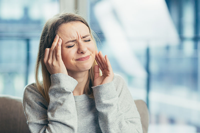 A woman who is clearly upset with a headache is massaging one temple with closed eyes 