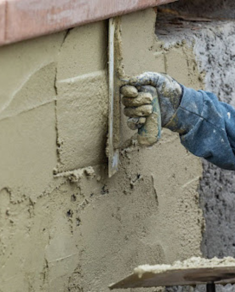 Foundation Repair Contractors in Astoria, NY - A Man Applying Cement to the Outside of a Foundation<br />
