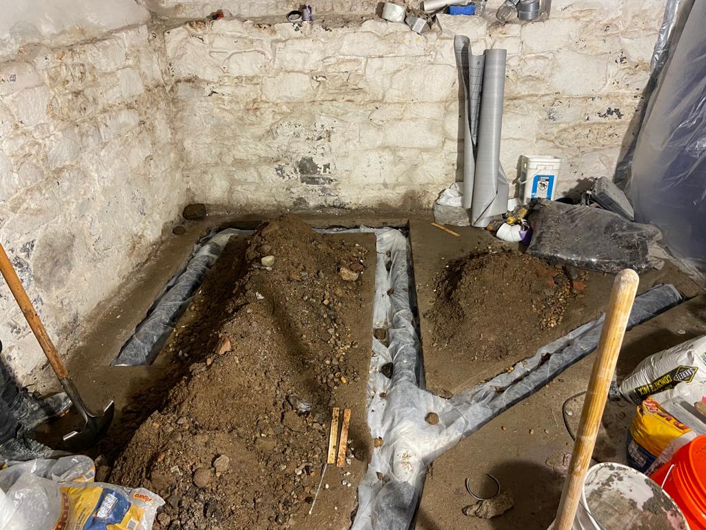 After diagnosing the issues, the team dug a space for laying the French drain pipe that would collect the basement water and channel it away.