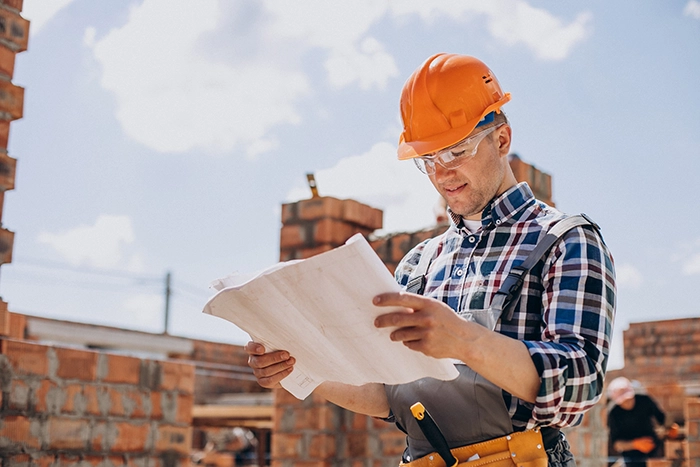 A Zavza Seal Contractor on a job site in an orange hard hat and orange reflective vest viewing the blueprint of the repair work.