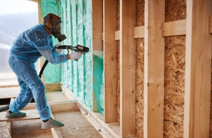 Closed cell spray insulation in progress by a contractor of zavza seal in protective overalls and a mask.