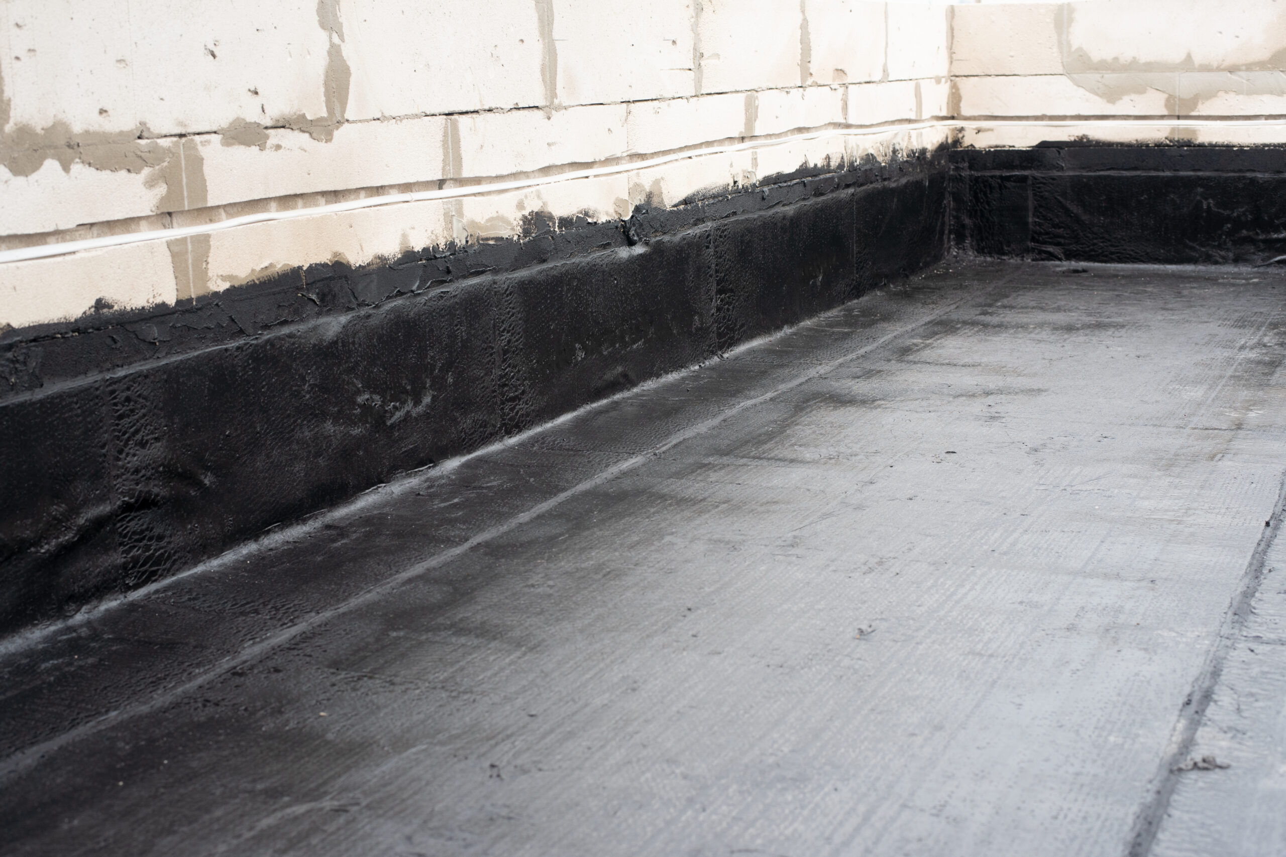 A black waterproofing adhesive spread on the floor of a basement 