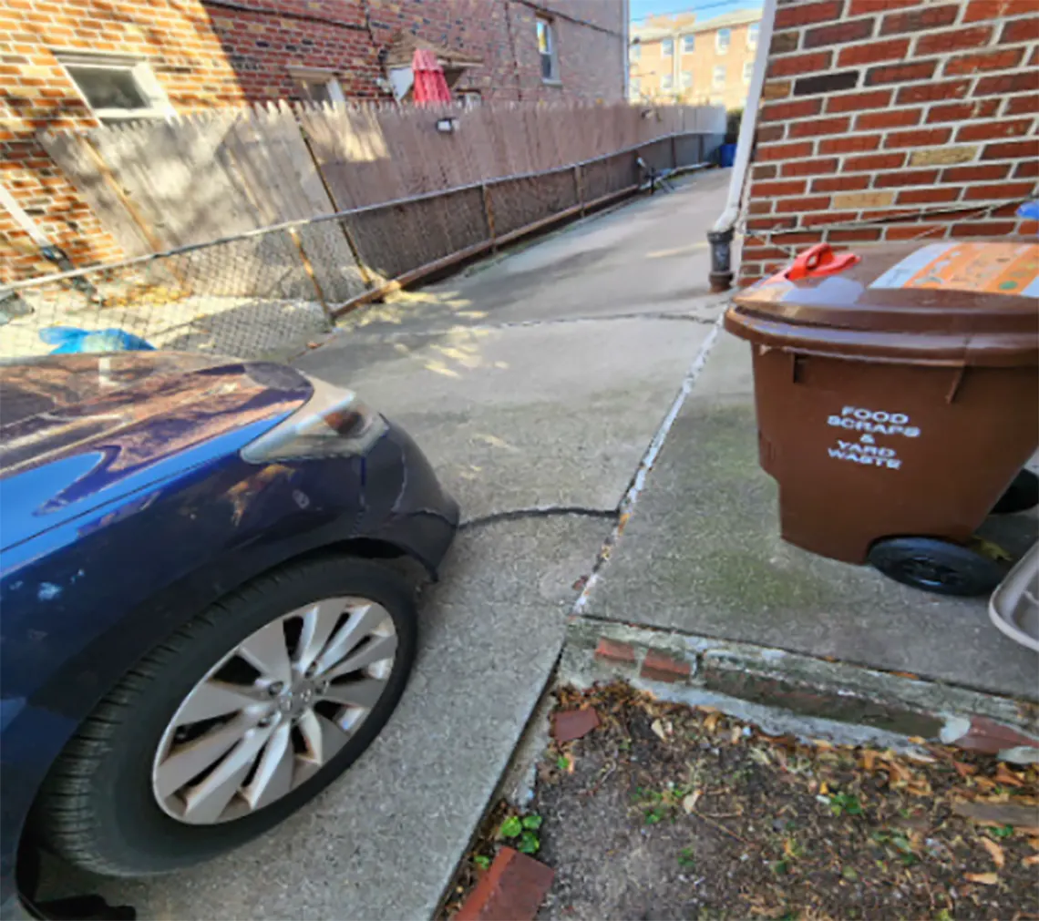 curb of the driveway that is cracked and sunken under the wheel of the parked car.