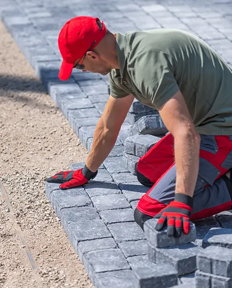 A contractor in a red sun hat is laying pavers in a driveway space