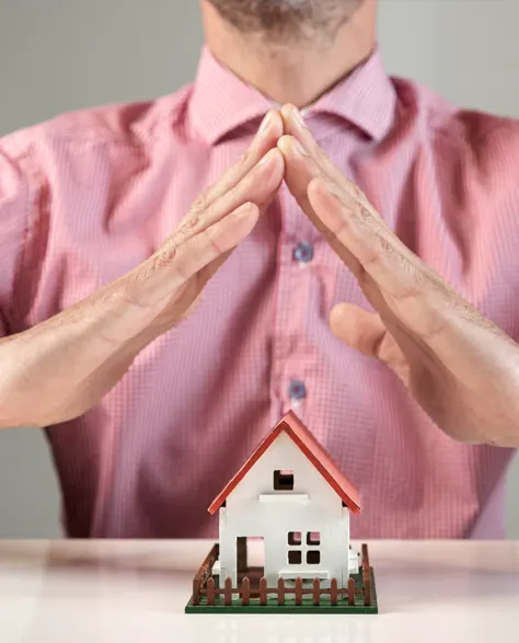 A man creating a roof with his hands over toy house depicting safety 