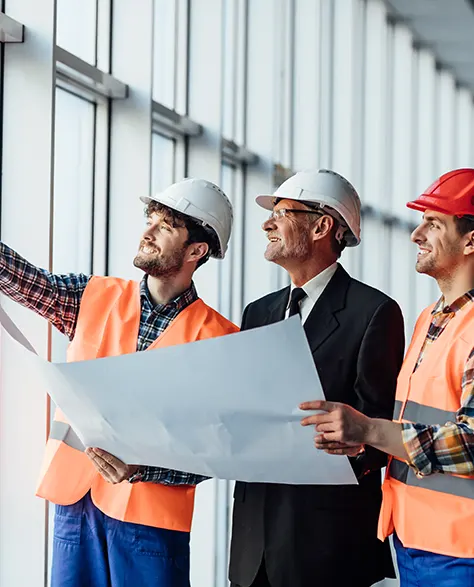 three contractors in hard hats standing in a building looking at a blueprint