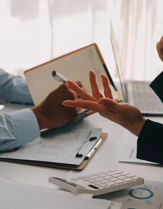 Two people having a conversation over a study table with clipboard, diary and papers<br />
