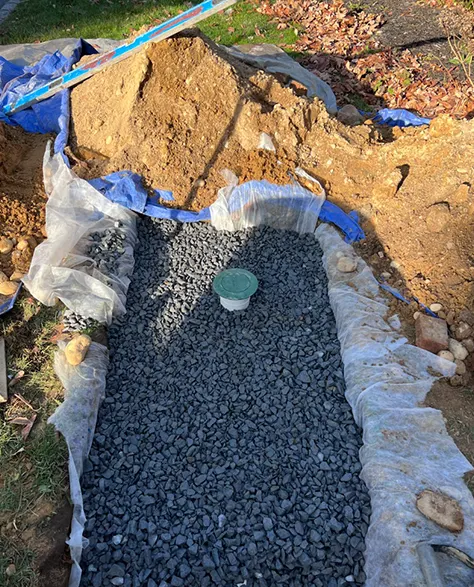 A newly installed catch basin where the pebbles on top will accumulate water and direct it to a controlled and closed basin underground that will lead to the main drainage.