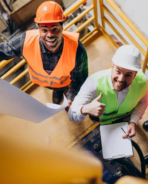 Two contractors in yellow hard hats are discussing lally column placement at a job site.