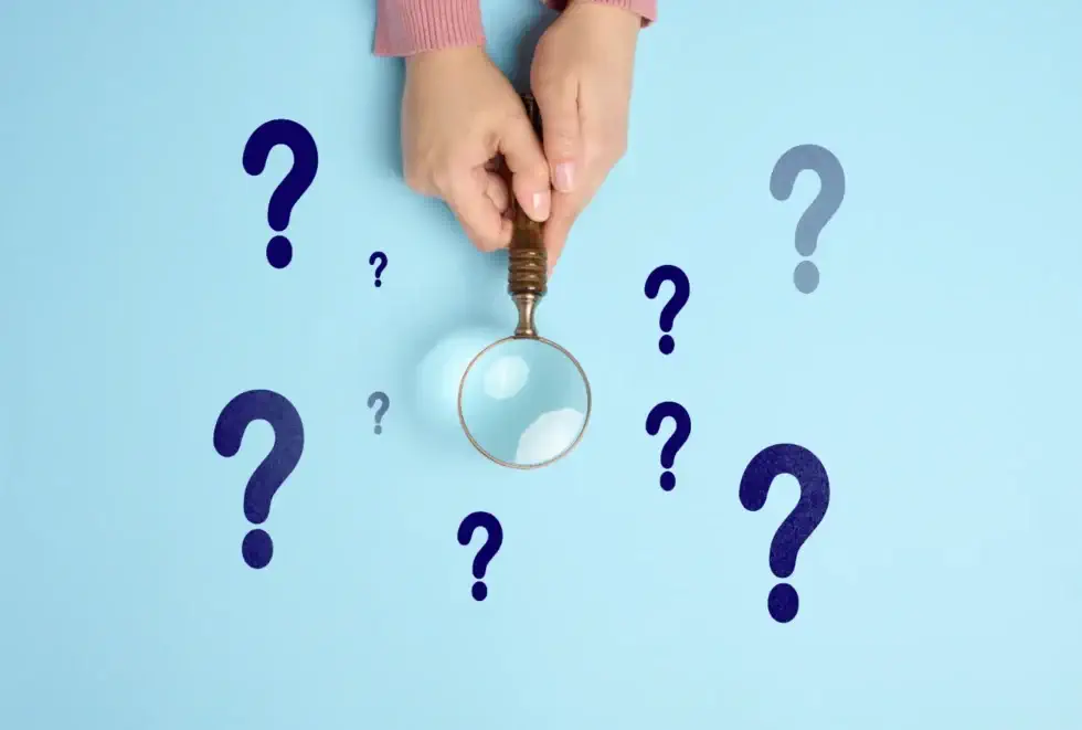What Types of Mold Are in a Crawl Space? - A Woman’s Hands Holding a Magnifying Glass Over a Light Blue Surface with Dark Blue Question Marks on it
