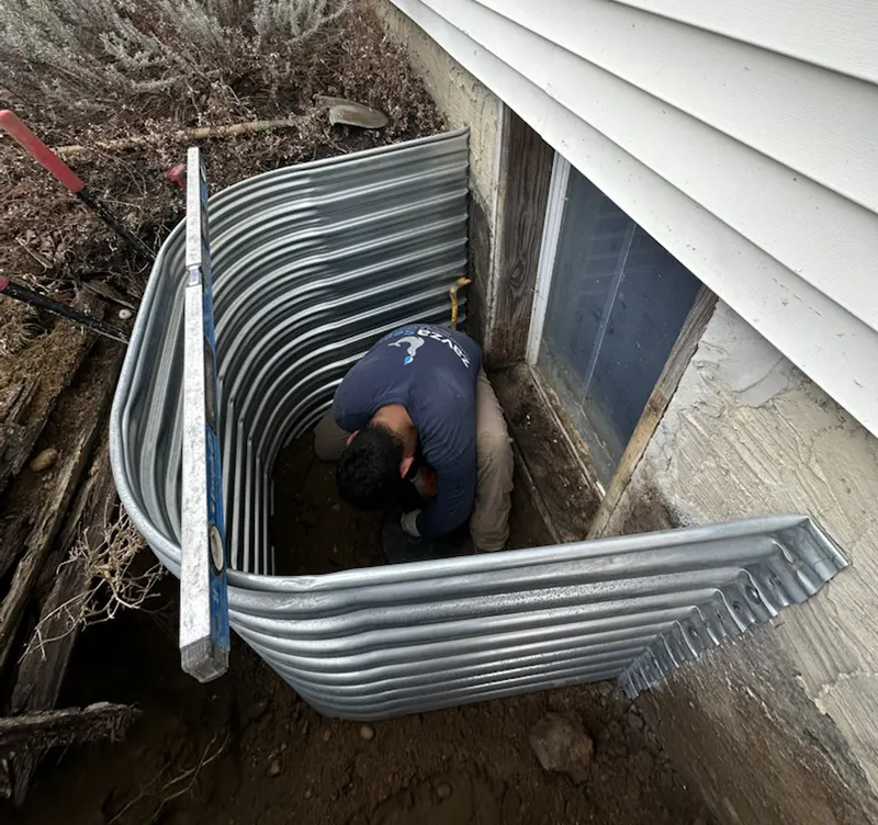 A man is installing an egress window in a basement.