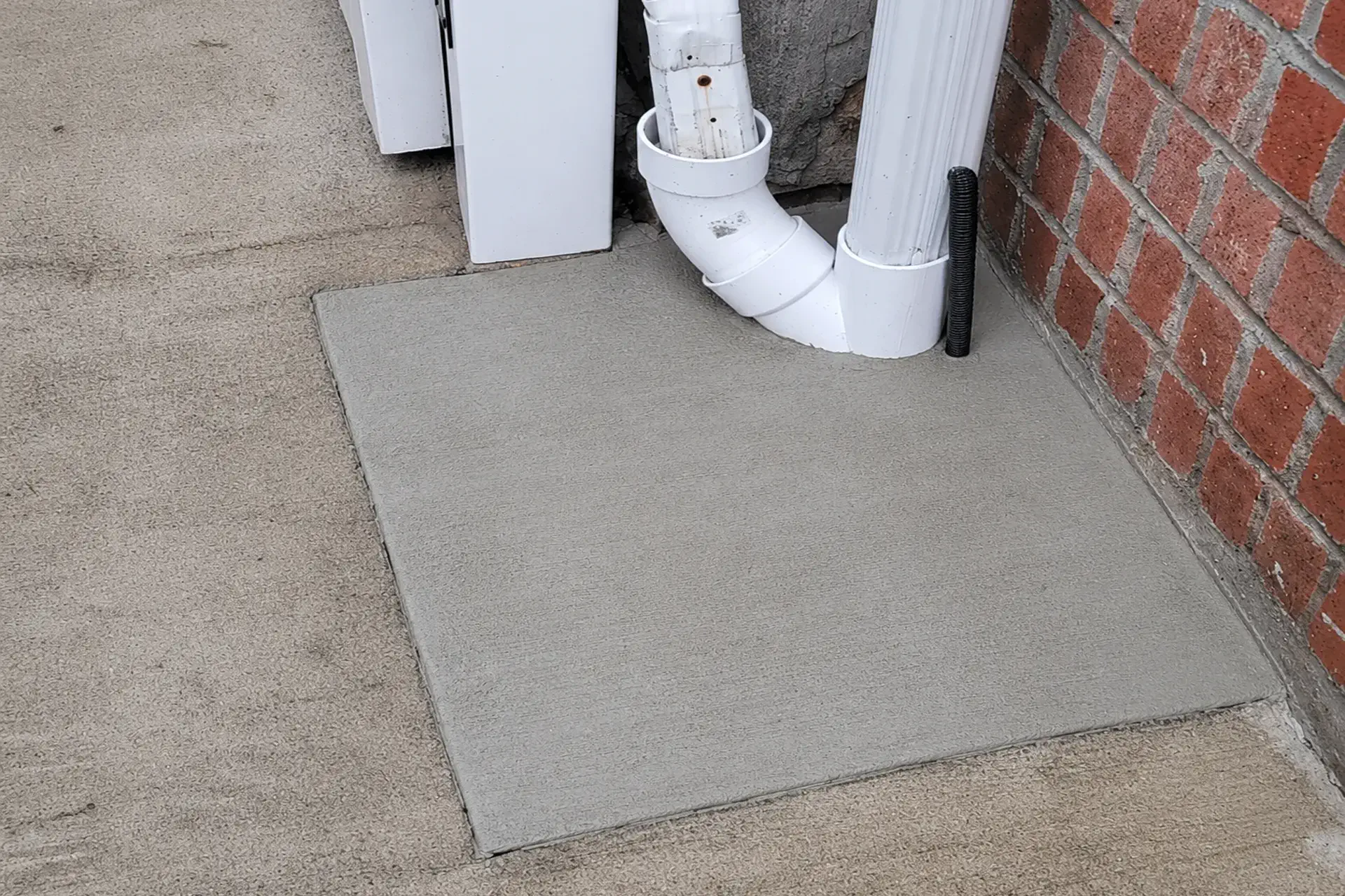 completed-downspout-drain-repair-featured Technician repairing a damaged underground PVC downspout drain beneath a concrete walkway during a residential drainage repair project in Flushing, NY.