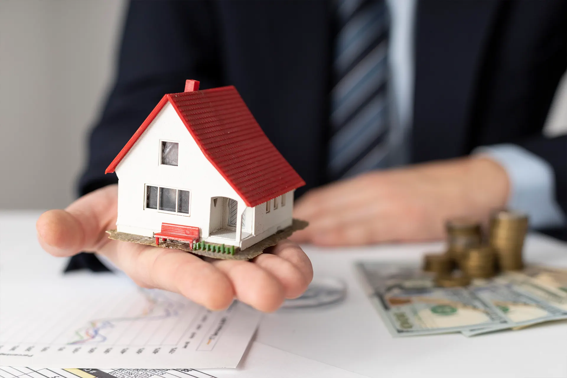 A man holding a toy house in his hand with money in the background showing the increase in property value<br />
